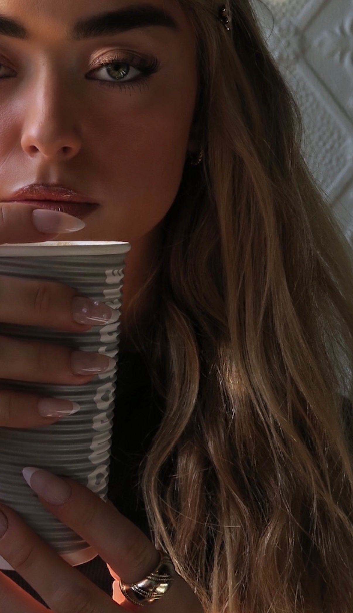 Woman holding a paper cup with a neutral background wearing French tip press on nails with pearl detail.