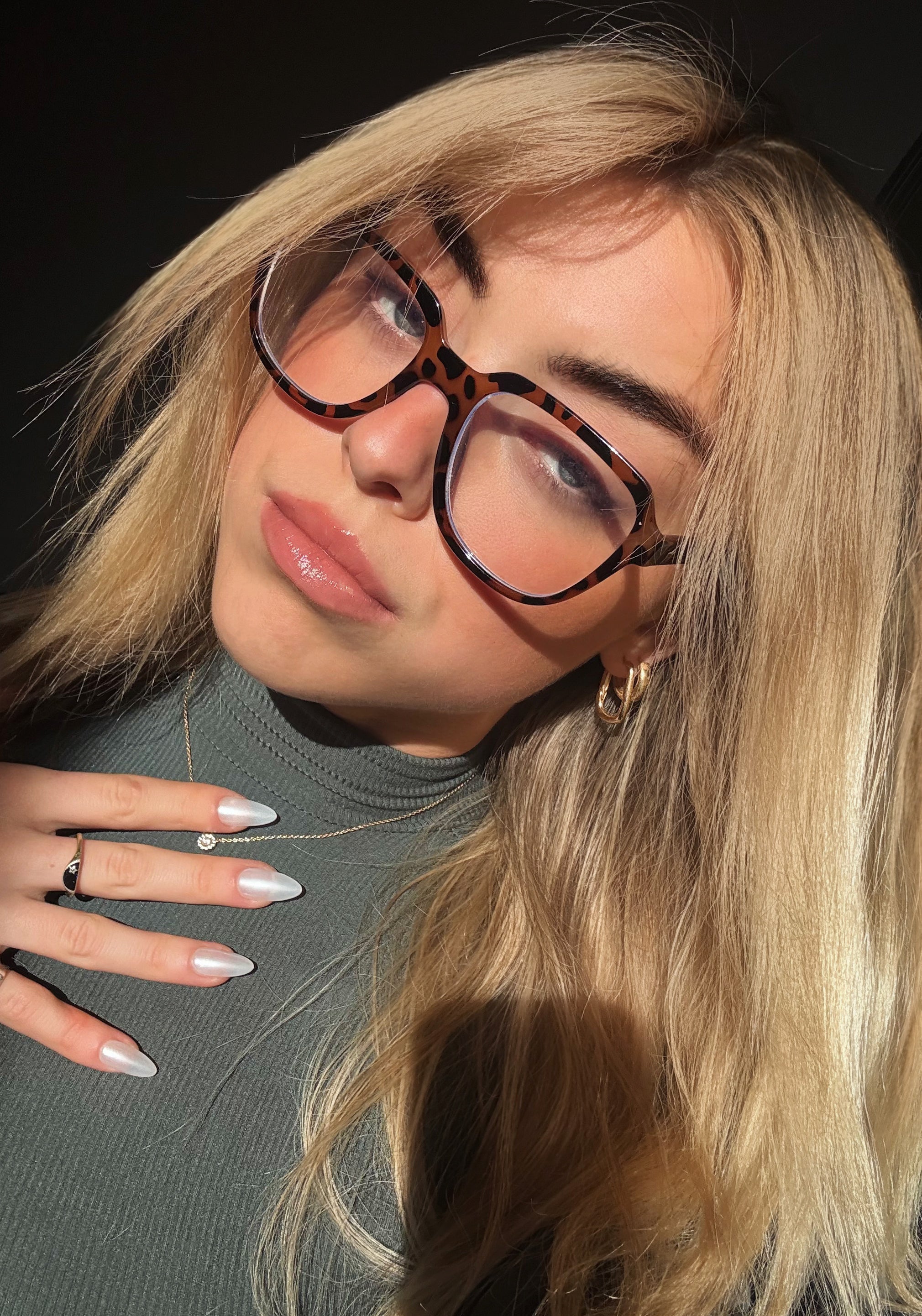Close-up of a person with blonde hair and glasses against a dark background wearing Sugar Tips Glass Slipper Pearl Chrome Glazed Donut Almond Press On Nails.
