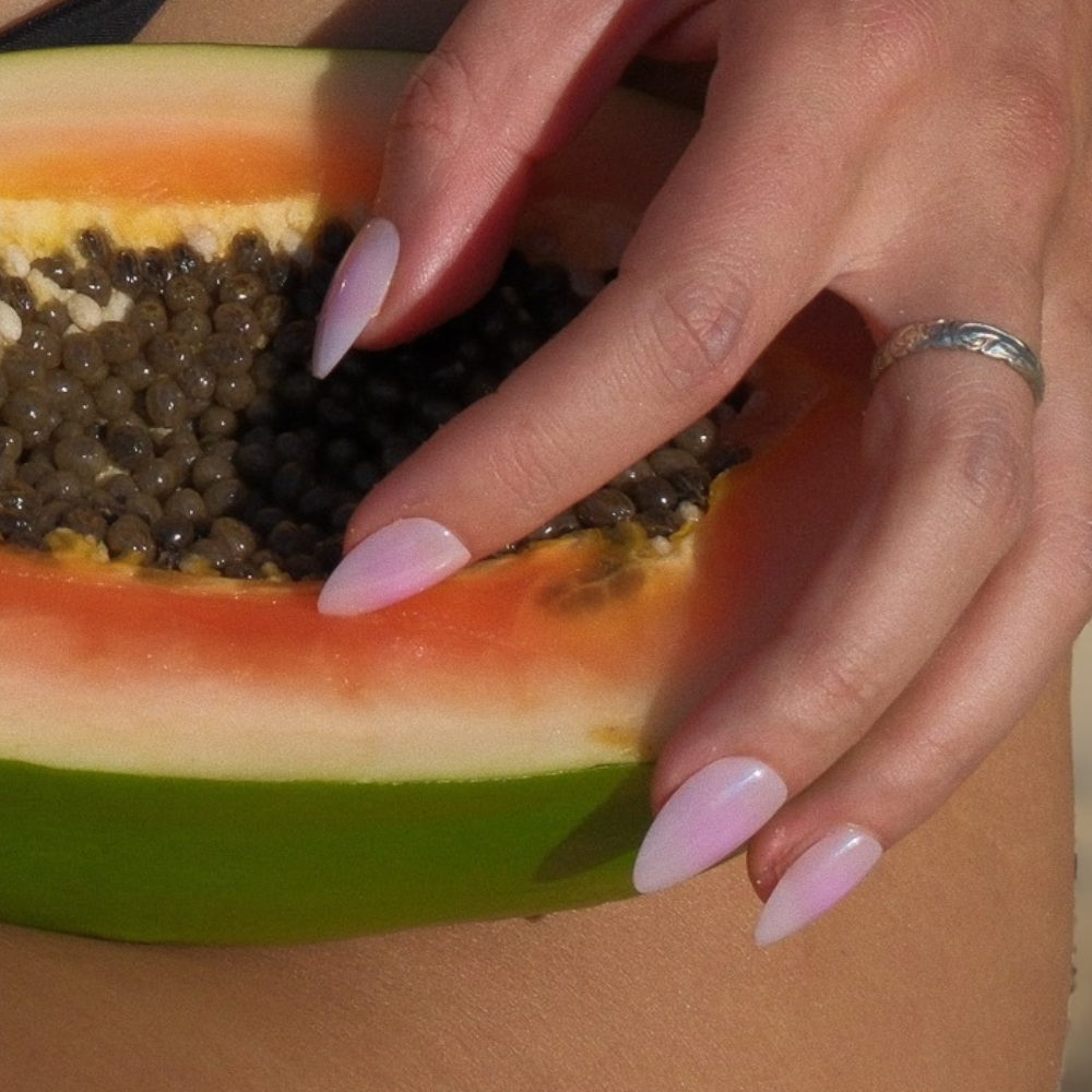 Cotton Candy pastel pink ombré almond press-on nails by Sugar Tips, holding a halved papaya in the sun