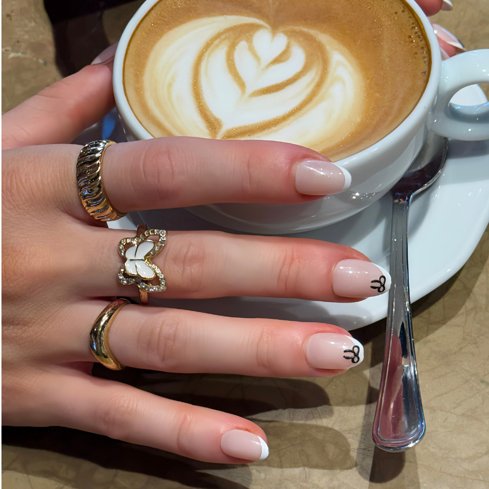 Hand holding a cup. Hand has Press on nails from Sugar Tips, French tip and small black bows