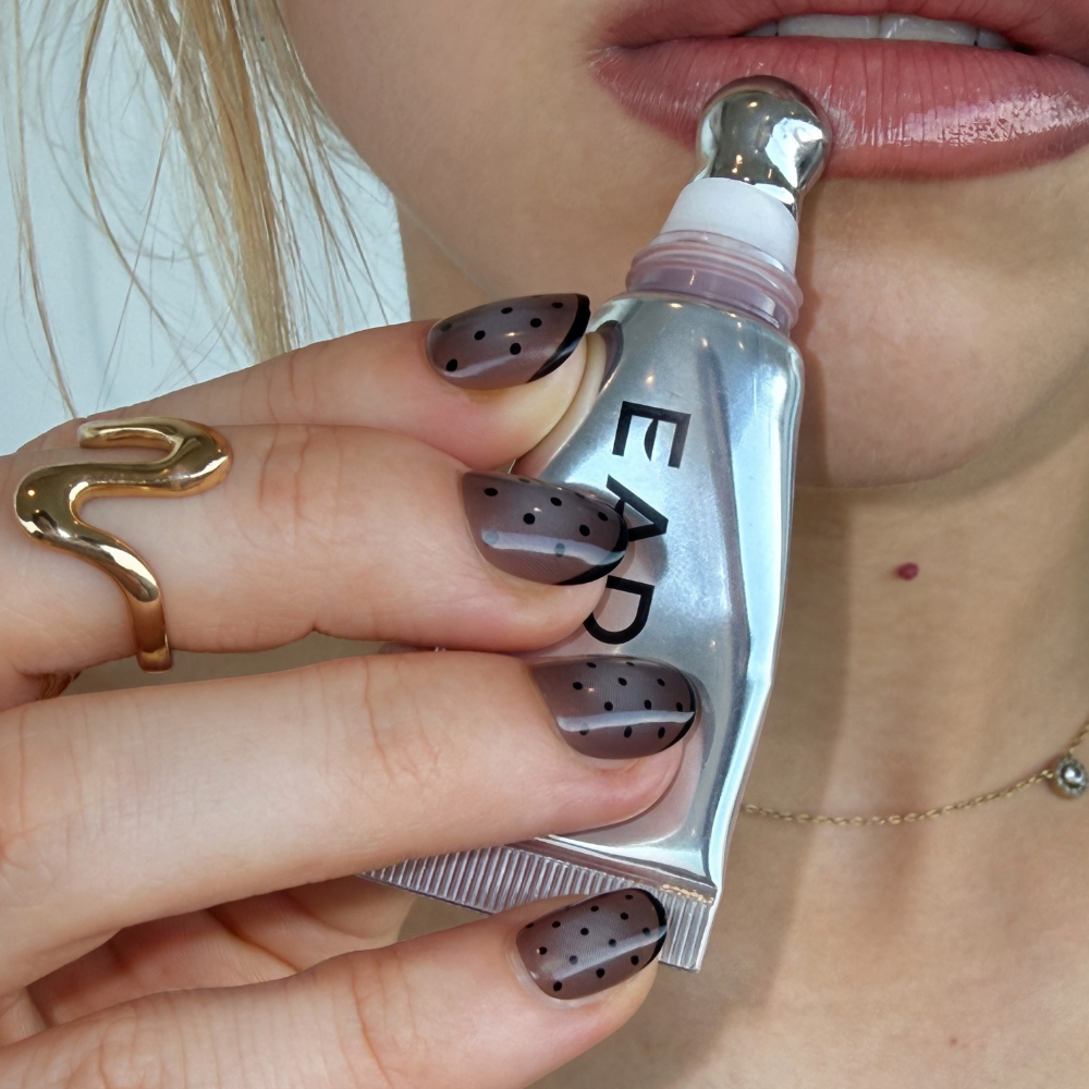 Handing applying lip gloss, wearing short black Pooka dot press on nails from sugar tips.