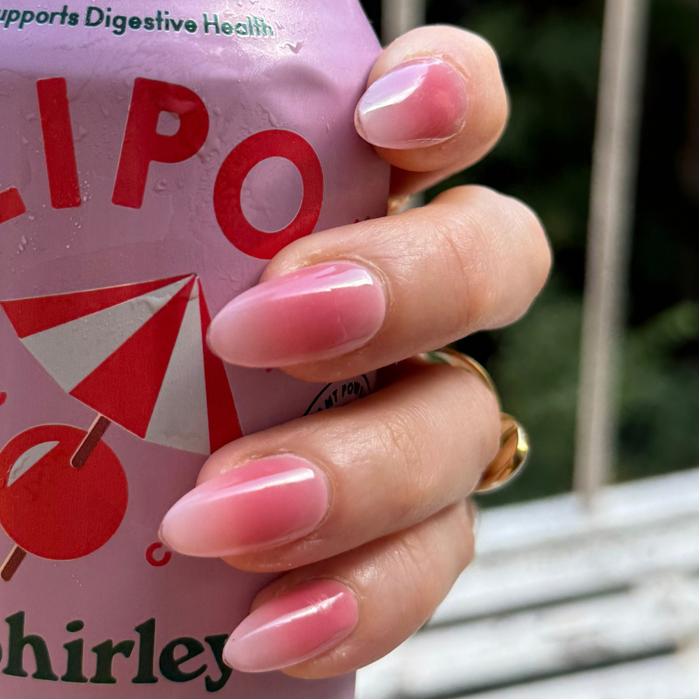 Close up of hand holding a pink soft drink can. Hand has press on nails from Sugar Tips, which are a pink ombré in long almond