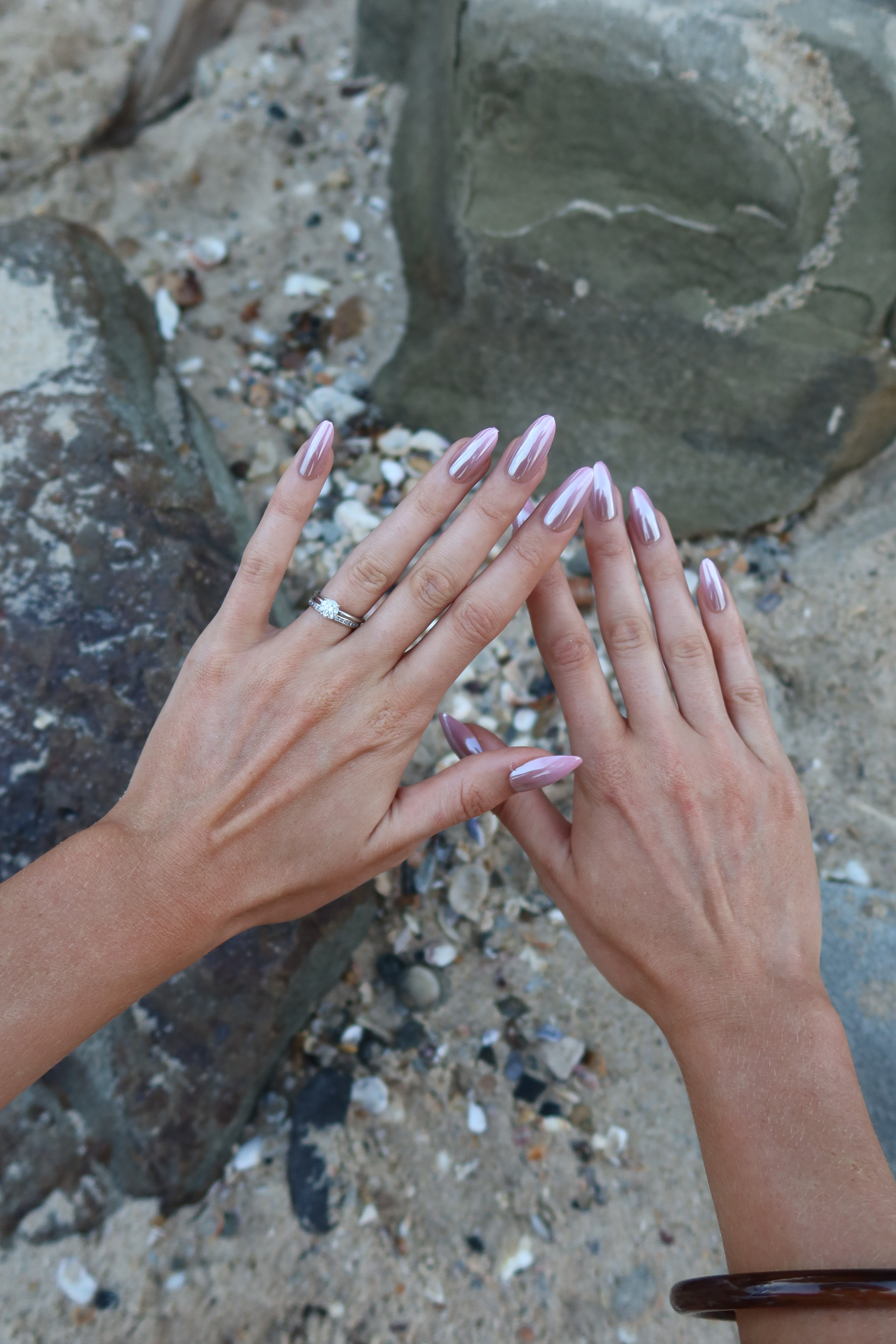Close-up of two hands with Sugar Tips Sorbet Crush Pink Ombre Almond press-on nails against a natural stone surface