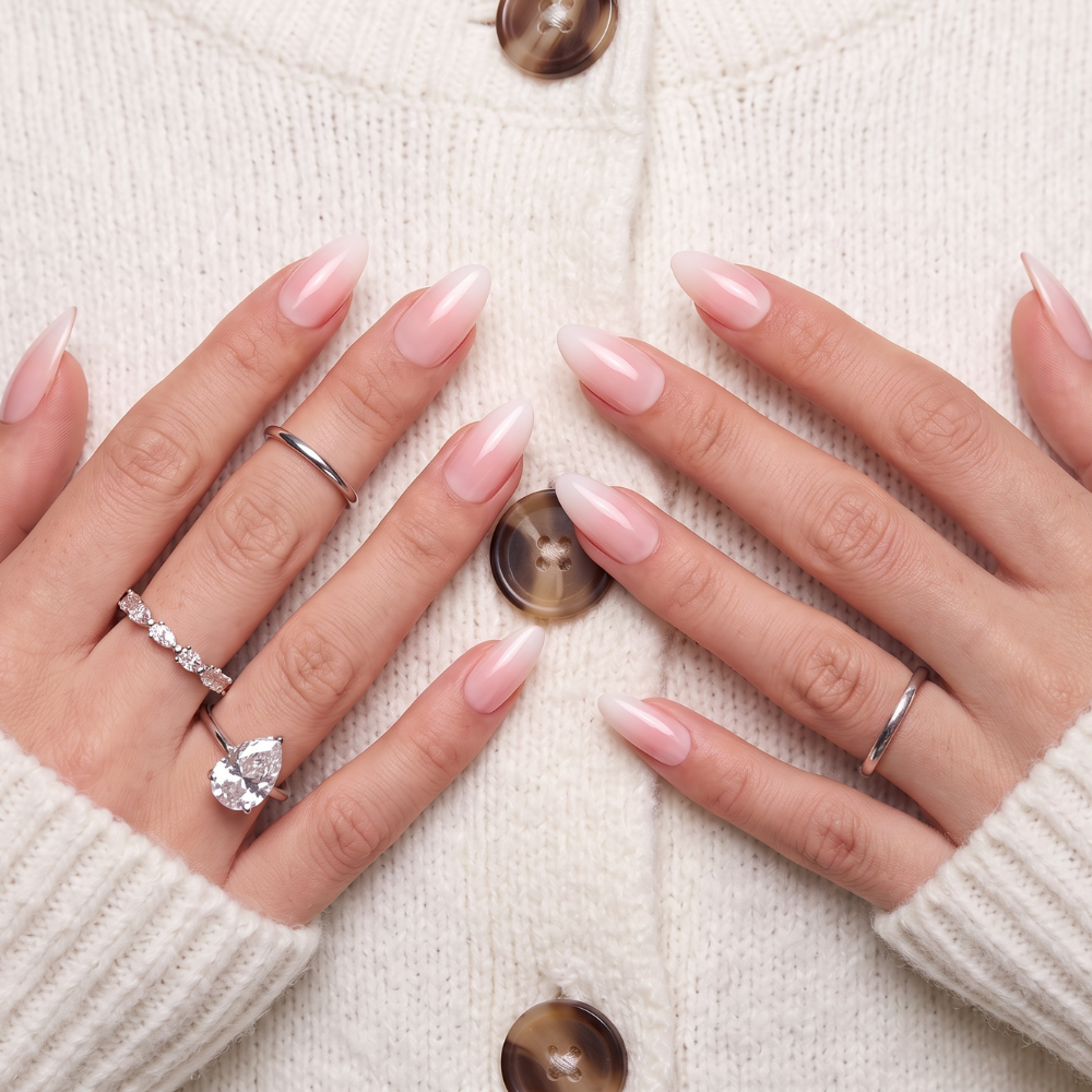 A woman holding their hands up to the chest, wearing Sugar Tips press on nails in a light pink Ombre 