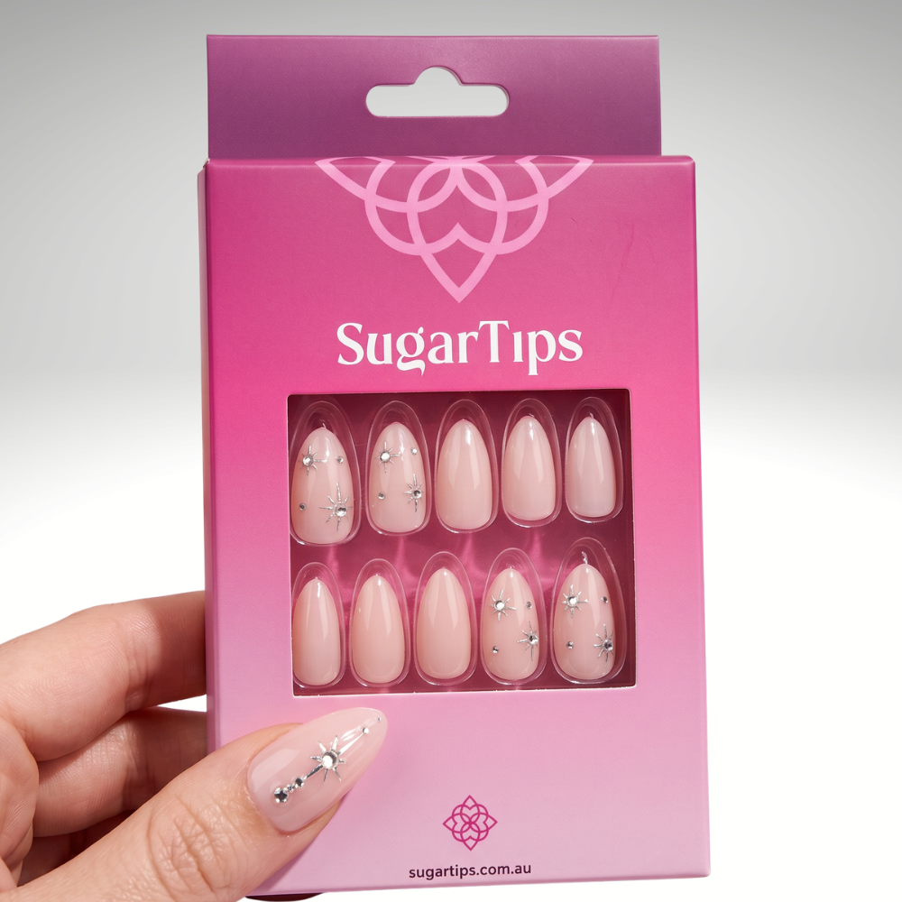 Hand holding a Sugar Tips press-on nail box, showing nude almond nails inside packaging — salon-quality press-on nails from $27.95