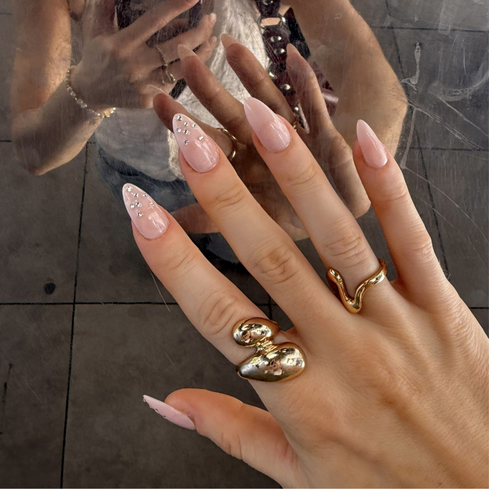 Woman's hand in natural sunlight showing pink almond press-on nails with rhinestone detailing and statement rings — Sugar Tips salon-quality press-on nails
