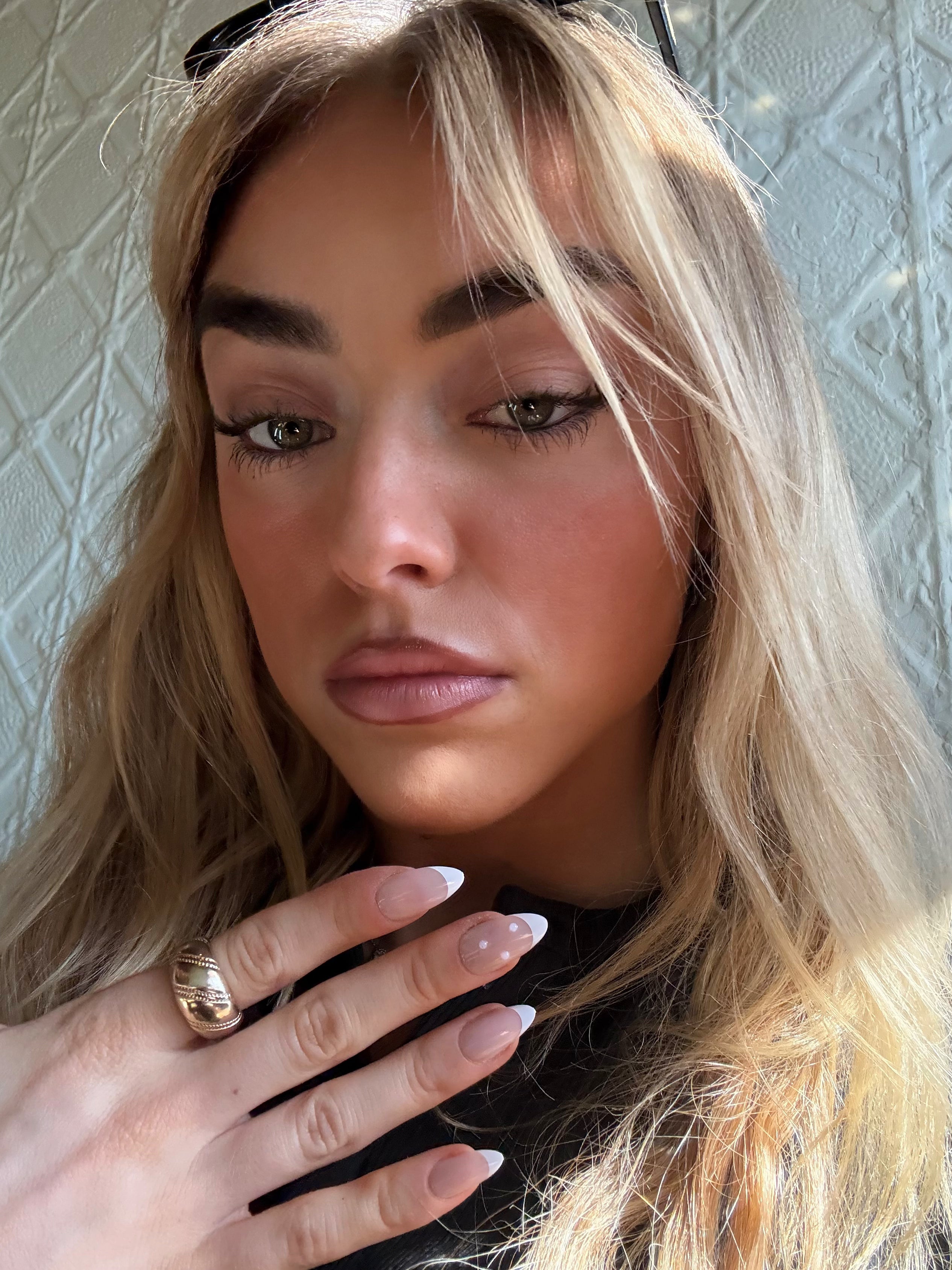 Close-up of a person wearing French tip press on nails with pearl detail with blonde hair and a textured wall background