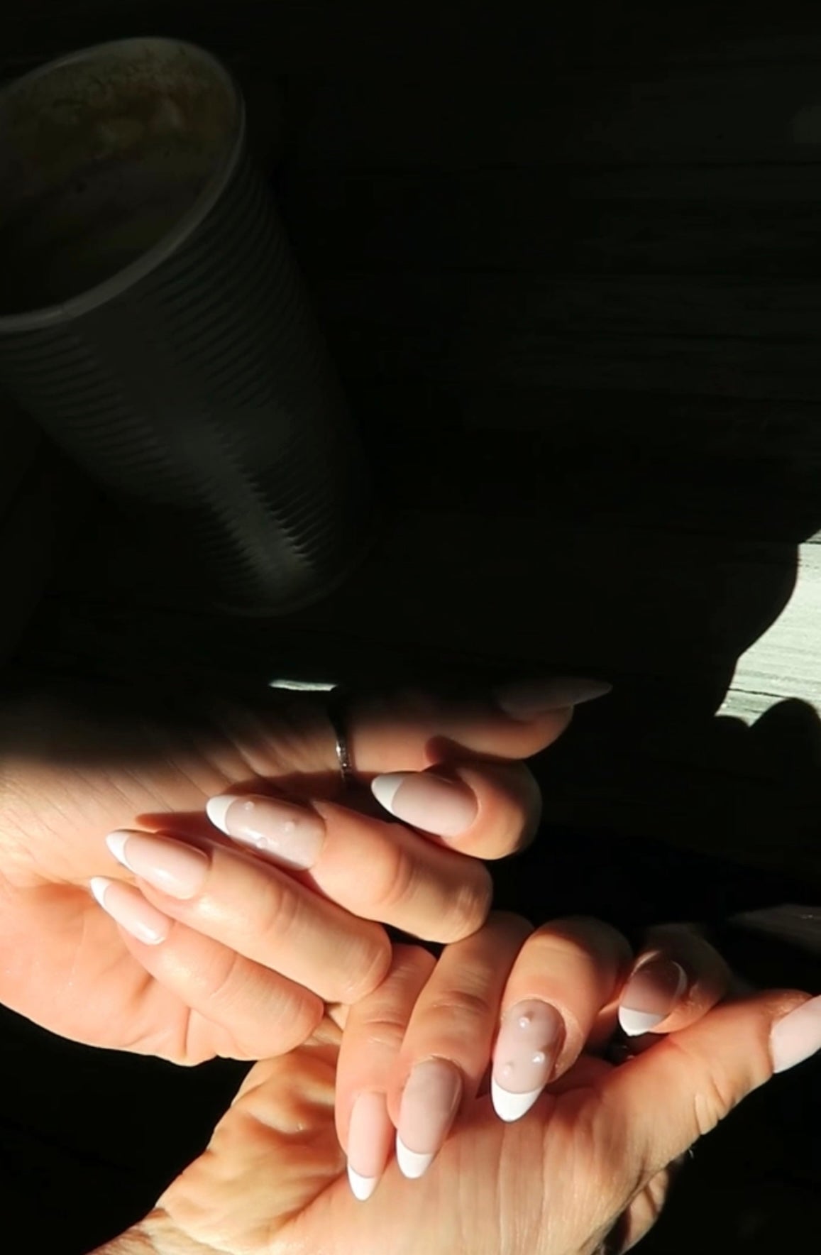 Close-up of two pairs of hands with light nail polish on press on nails a dark background