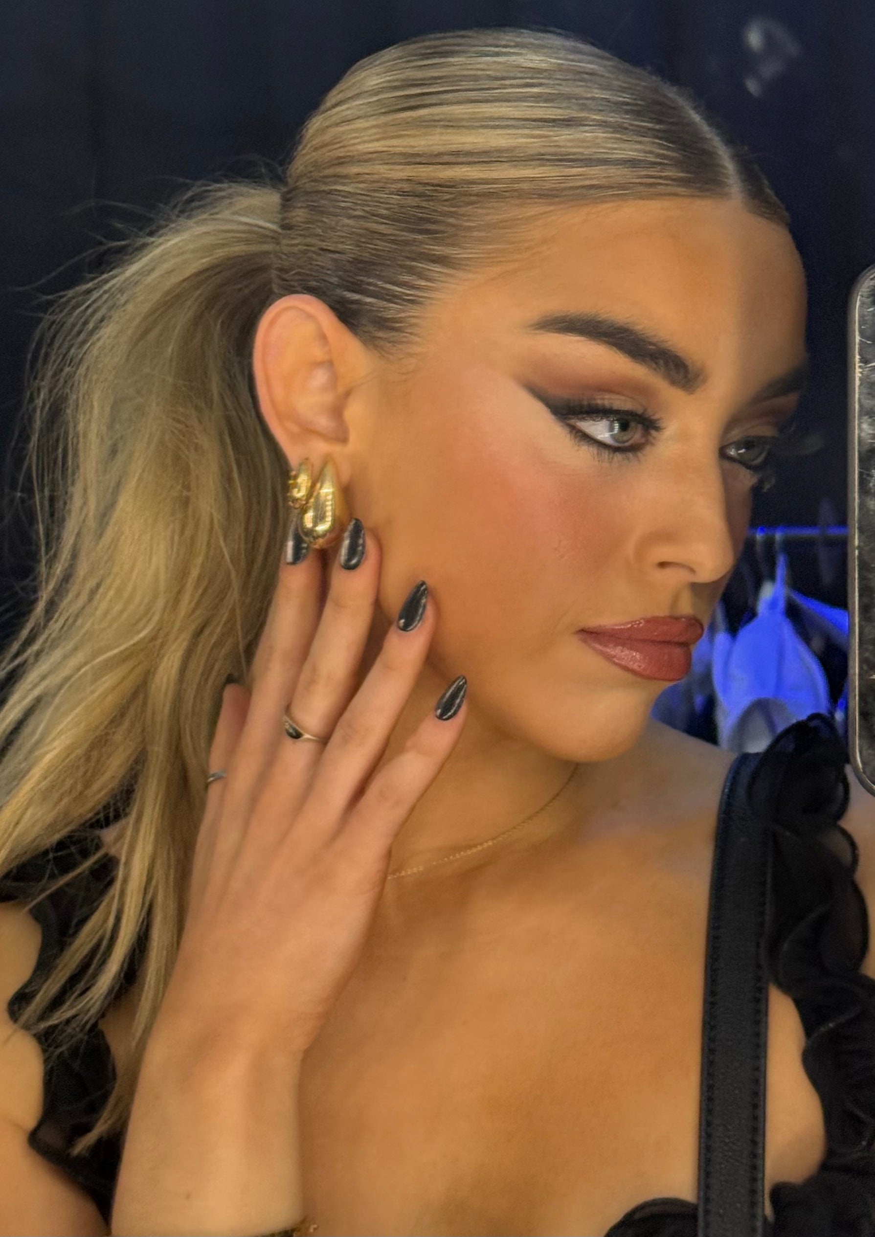 Woman adjusting her gold earring with a blurred background wearing Sugar Tips Midnight Kiss Metallic Silver Chrome Almond press on nails