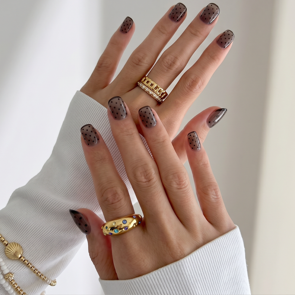 Sheer Nights short squoval press-on nails in smoky sheer taupe with dark polka dot details, styled with gold rings and bracelet — Sugar Tips Australia