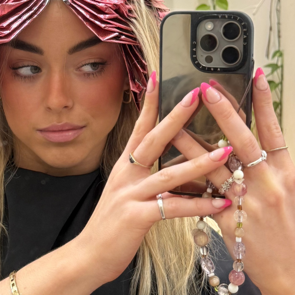 Barbie French neon pink French tip almond press-on nails by Sugar Tips, holding a phone with a beaded charm
