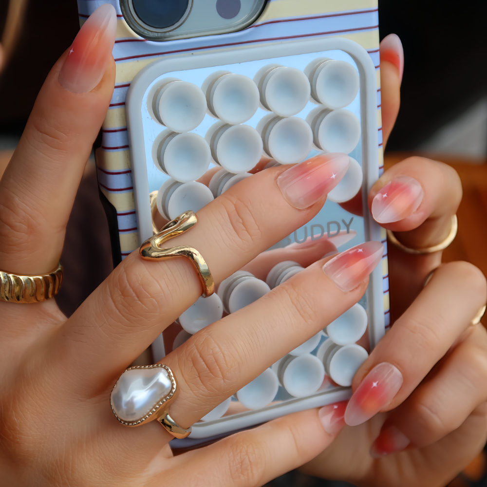 Hands are shown holding a mobile phone wearing peach ombré with small star detail, press on nails from sugar tips.