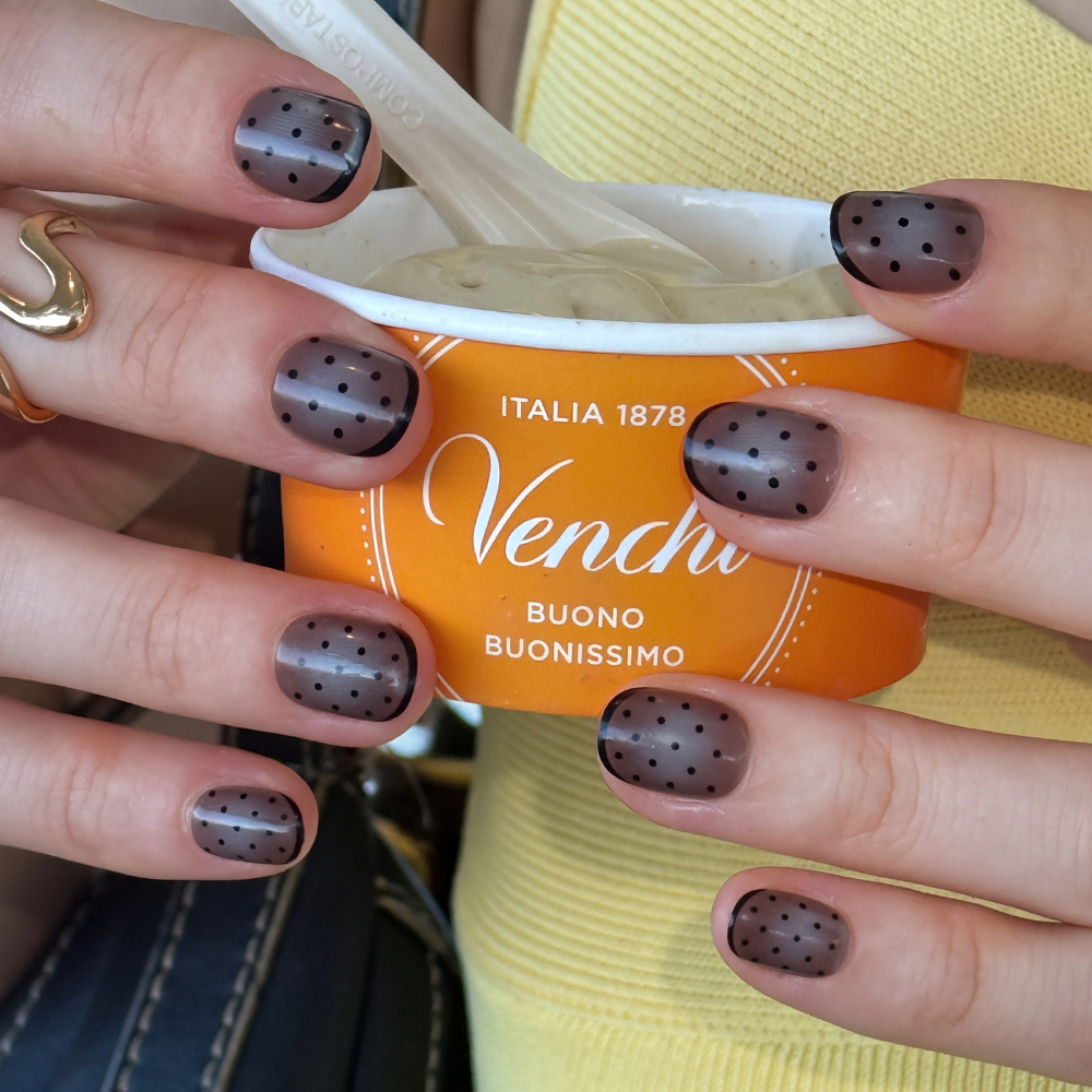 Close up of hand holding a cup of ice cream. Hand is showing press on nails from sugar tips in a dark spot pooka dot style 