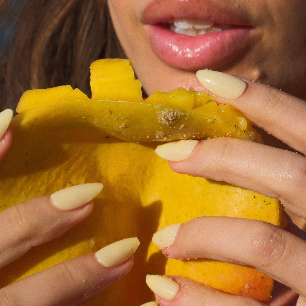 Close-up of a person peeling a mango with a focus on the hands, which are wearing yellow press on nails.