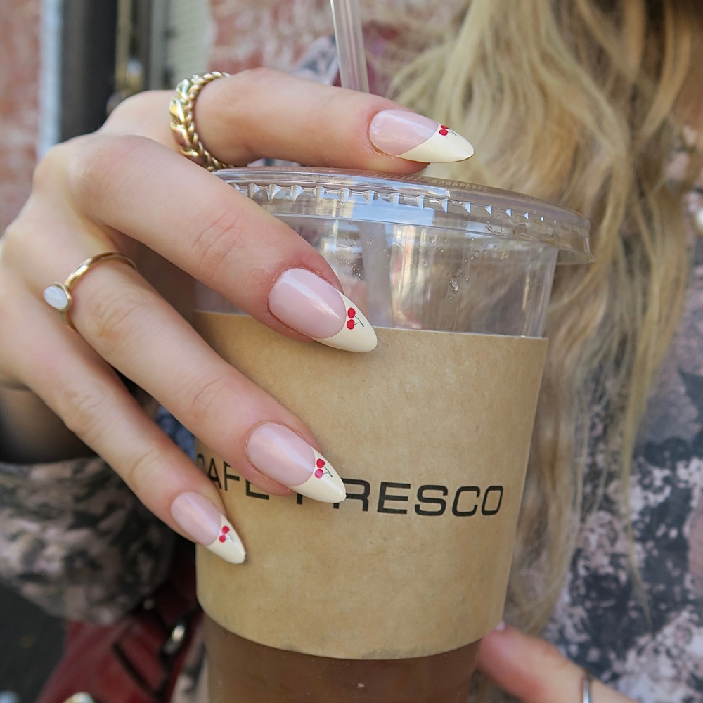 Hand holding a coffee cup with, featuring a French tip polish with cherry details.